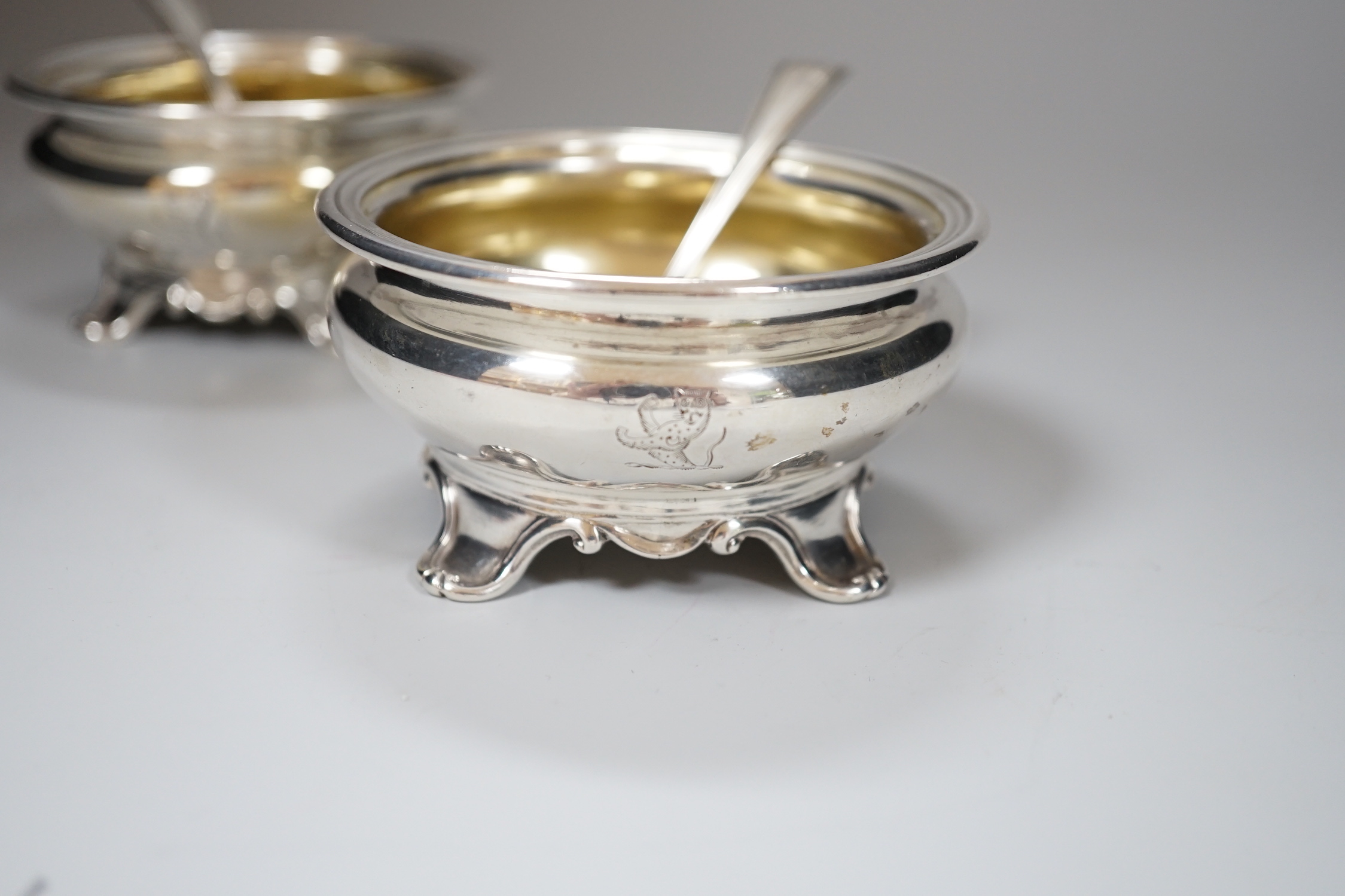 A pair of Victorian circular silver salts, with crests and scroll feet, makers Edward Barnard & Sons, London 1839, 207 grams, and a pair of George IV silver salt spoons, London 1827, 19 grams